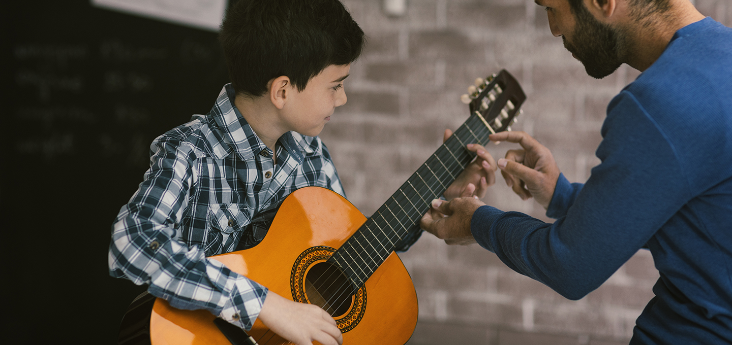 child playing guitar with instructor helping