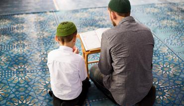 Boy at Mosque reading Koran with parent or teacher